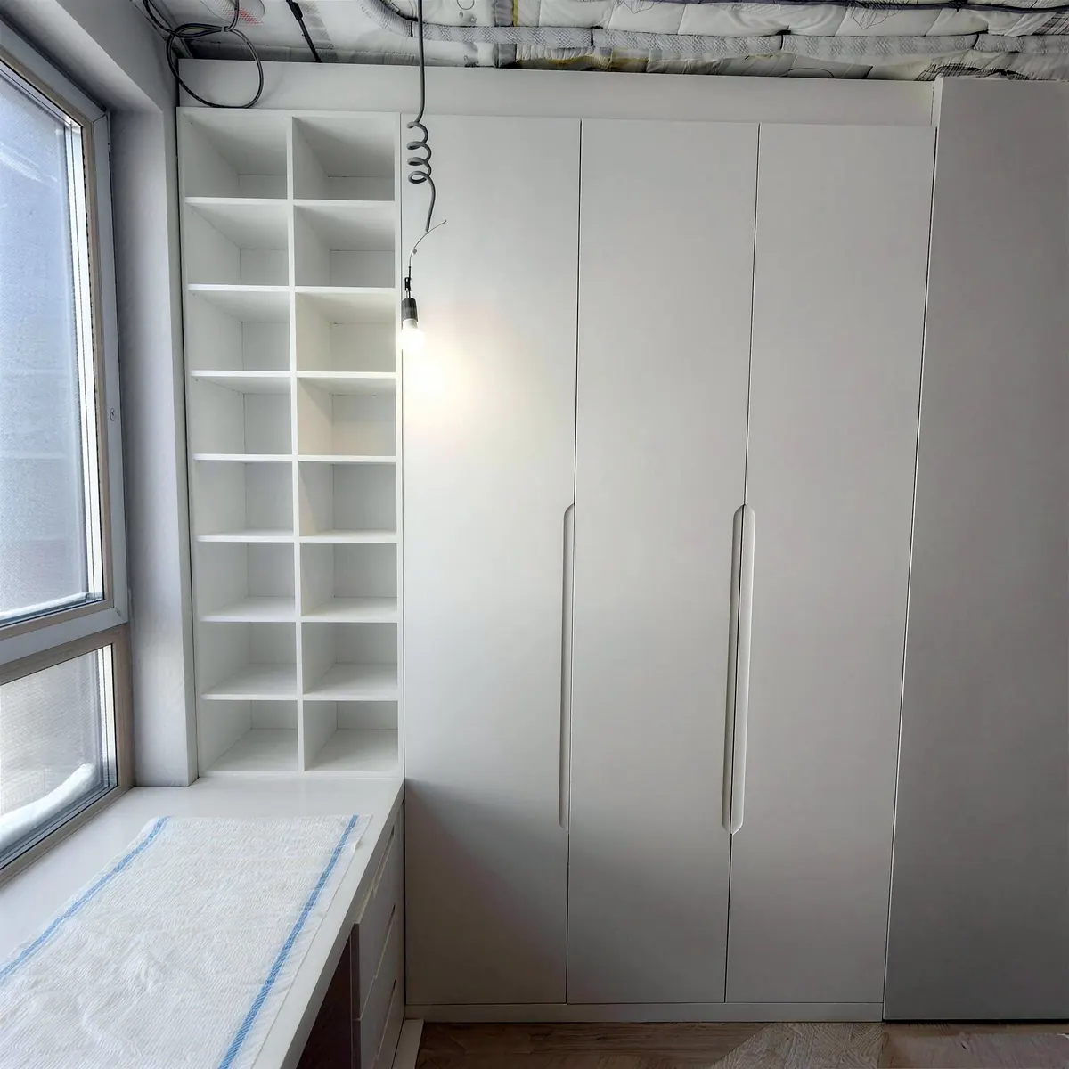Built-in white wardrobe and shelving next to a window seat