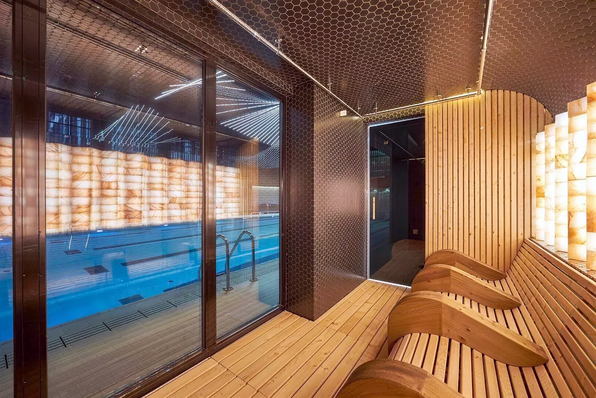 Spa lounge with wood loungers, a salt wall and the pool behind glass