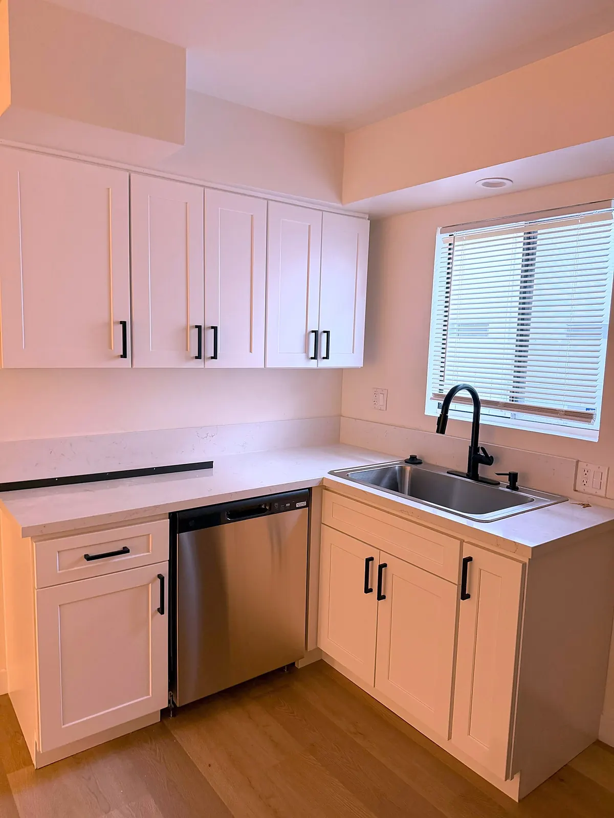 Small kitchen with white shaker cabinets, quartz counters and a black faucet under the window