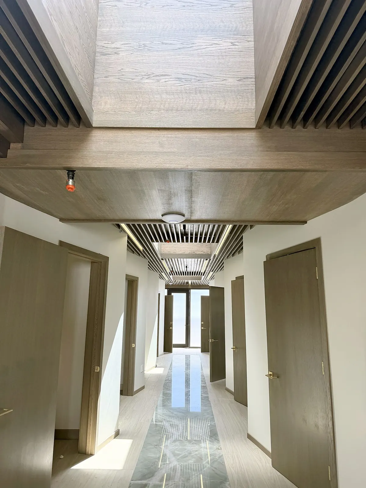 Medical office corridor with a wood-slat ceiling, skylight and marble-look floor