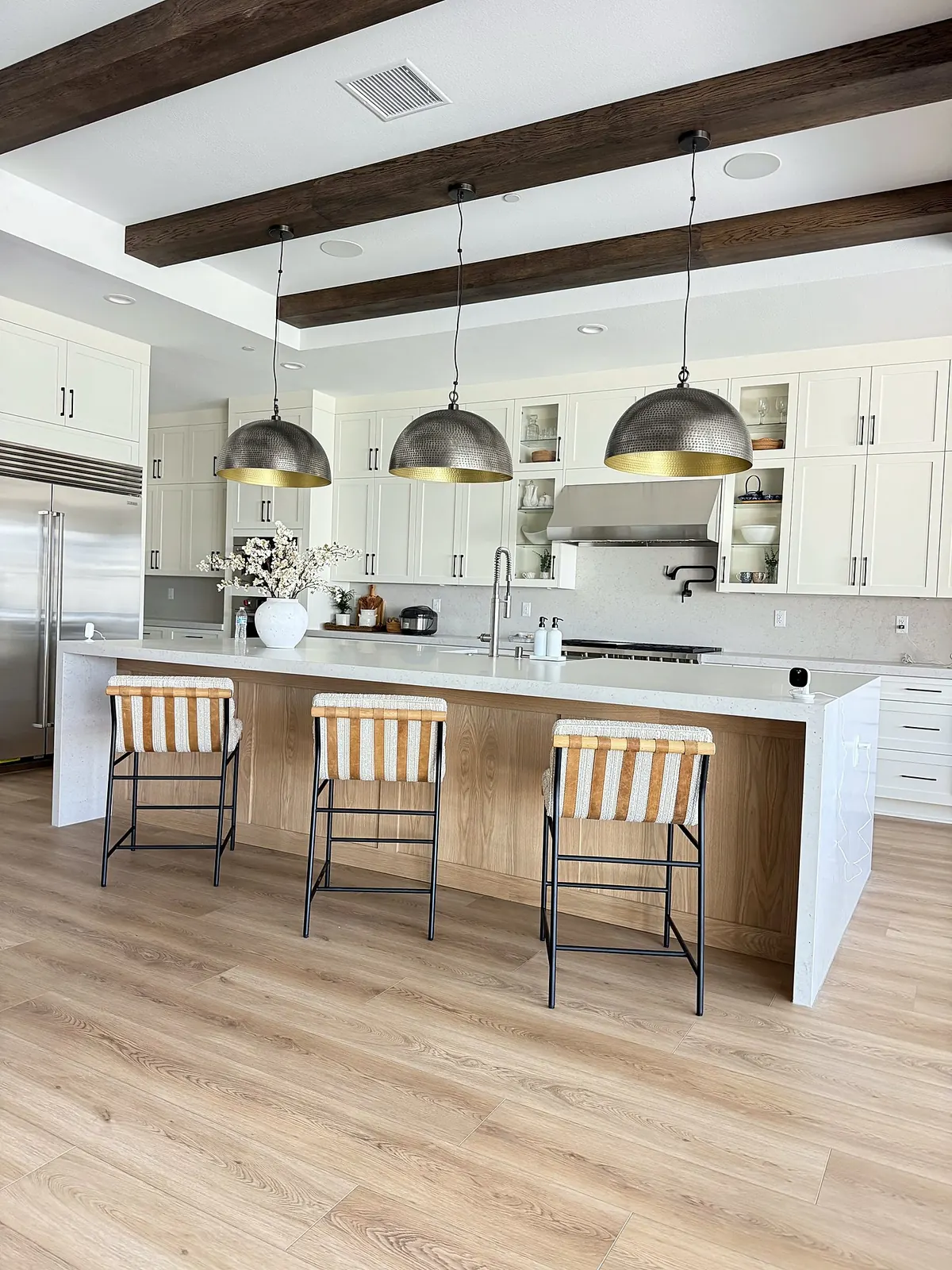 Kitchen island with brass pendants under wood ceiling beams in Porter Ranch